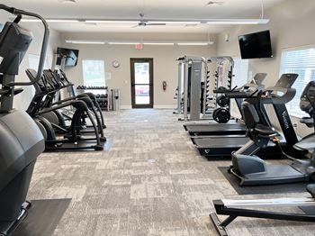 a gym with cardio equipment and a tv